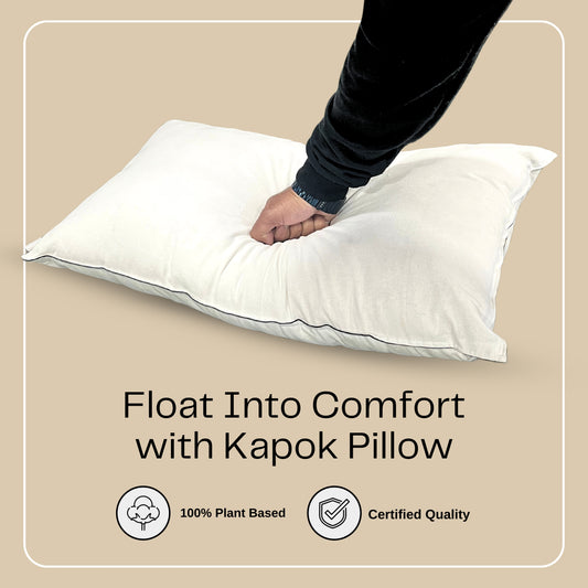 A plush king-size kapok pillow being pressed by a hand to demonstrate its softness and resilience. The image features the text 'Float Into Comfort with Kapok Pillow' on a beige background, highlighting key features such as 100% plant-based materials and certified quality. Ideal for those looking to buy king kapok pillows online for superior comfort and support.